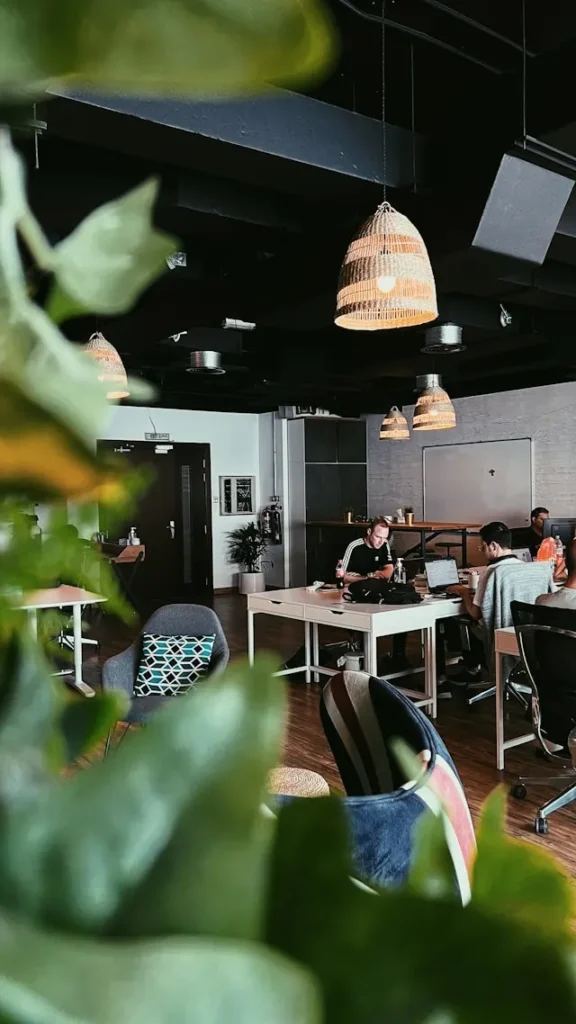 Professionals working on laptops in a modern, warm-lit open office space, representing a collaborative digital agency environment.